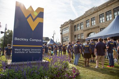 A large group of people mingle in front of Carter Hall with the WVU Beckley Campus sign in the foreground.